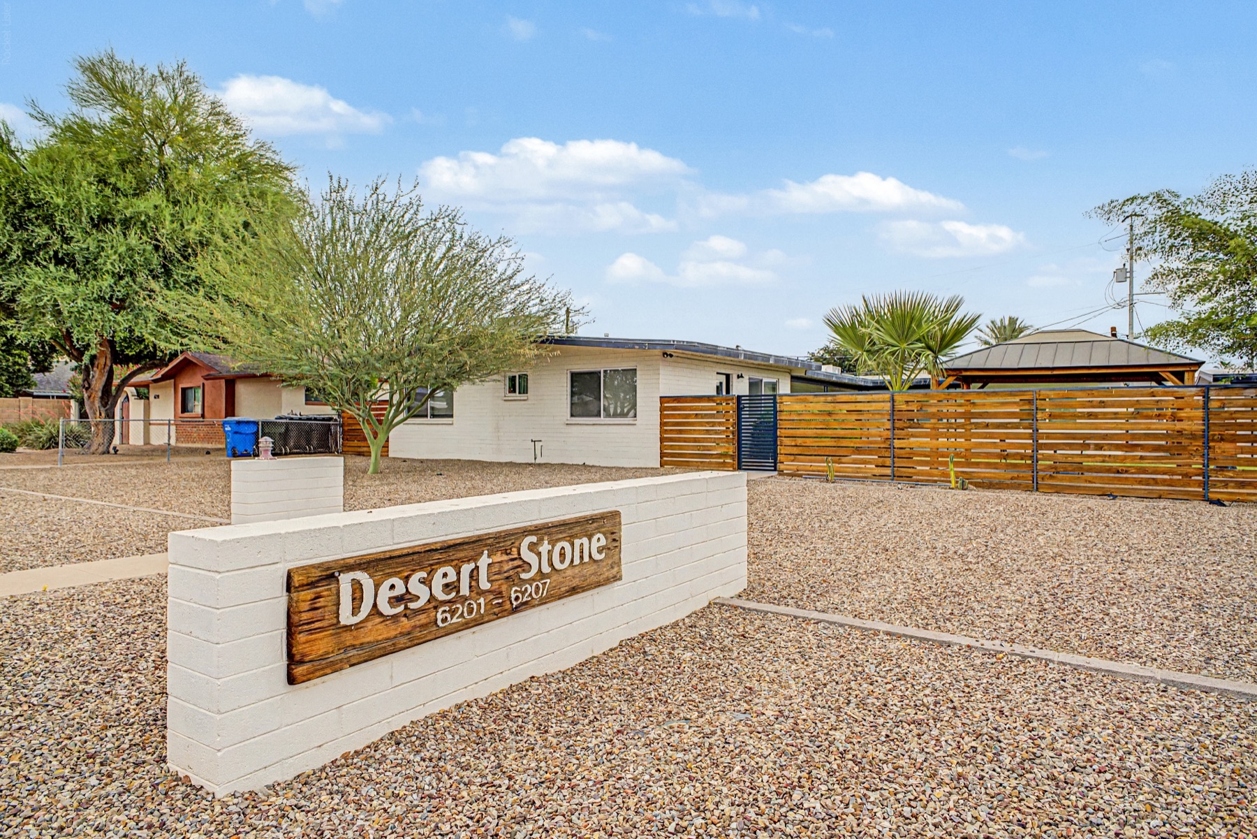 Desert Stone entrance sign marked 6201 and 6207, with low-rise buildings, trees and gravel landscaping beyond.